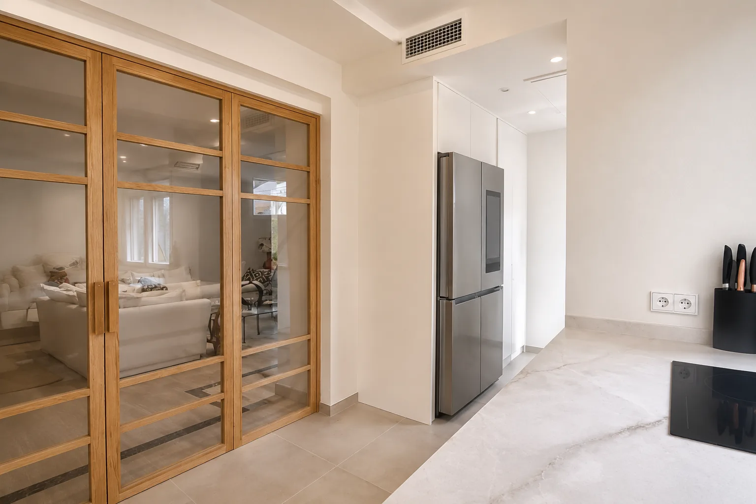 Una cocina en cashmere conectada al salón con madera y cristal