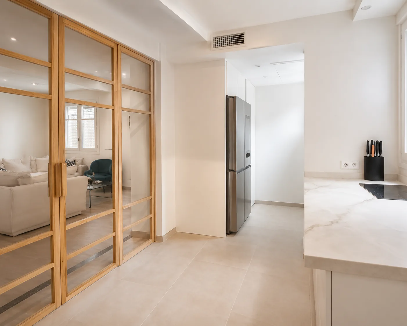 Una cocina en cashmere conectada al salón con madera y cristal