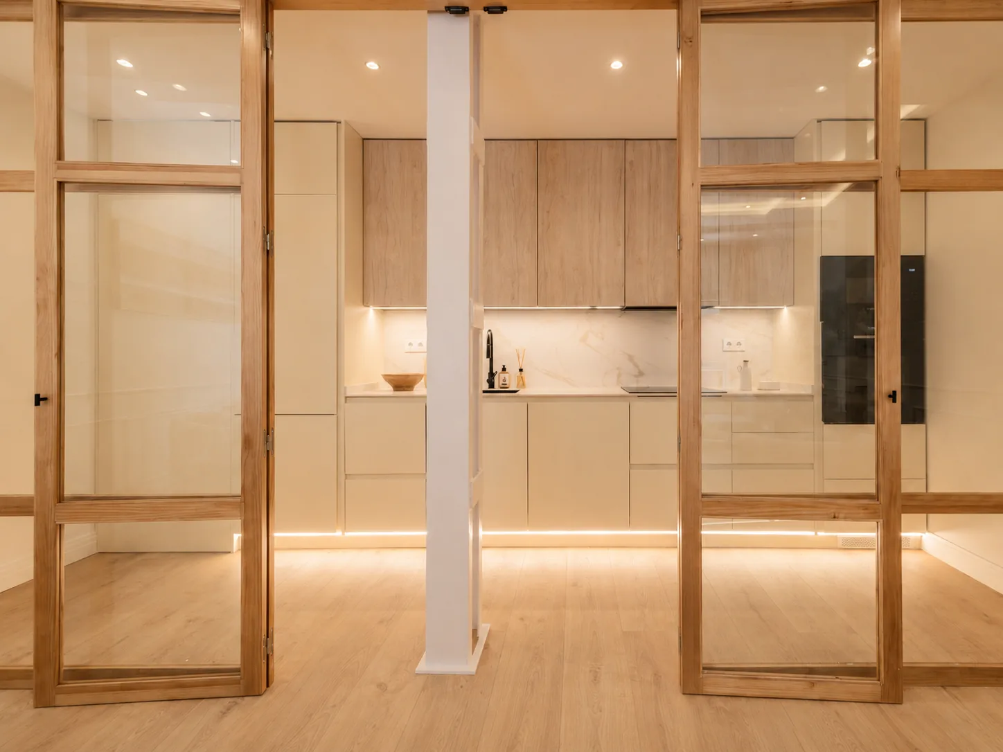 Cocina integrada en el pasillo con acabados en madera clara y crema