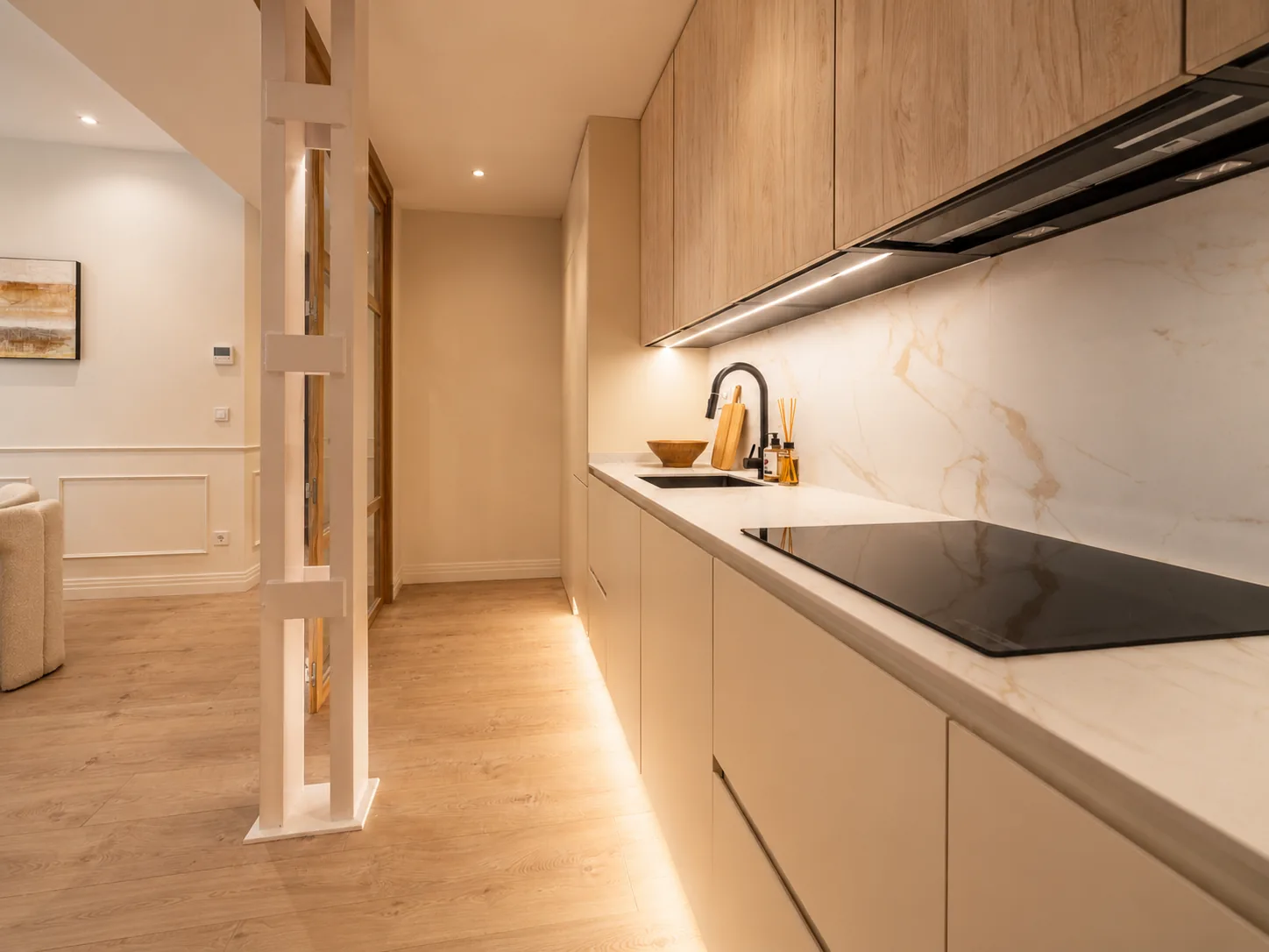 Cocina integrada en el pasillo con acabados en madera clara y crema