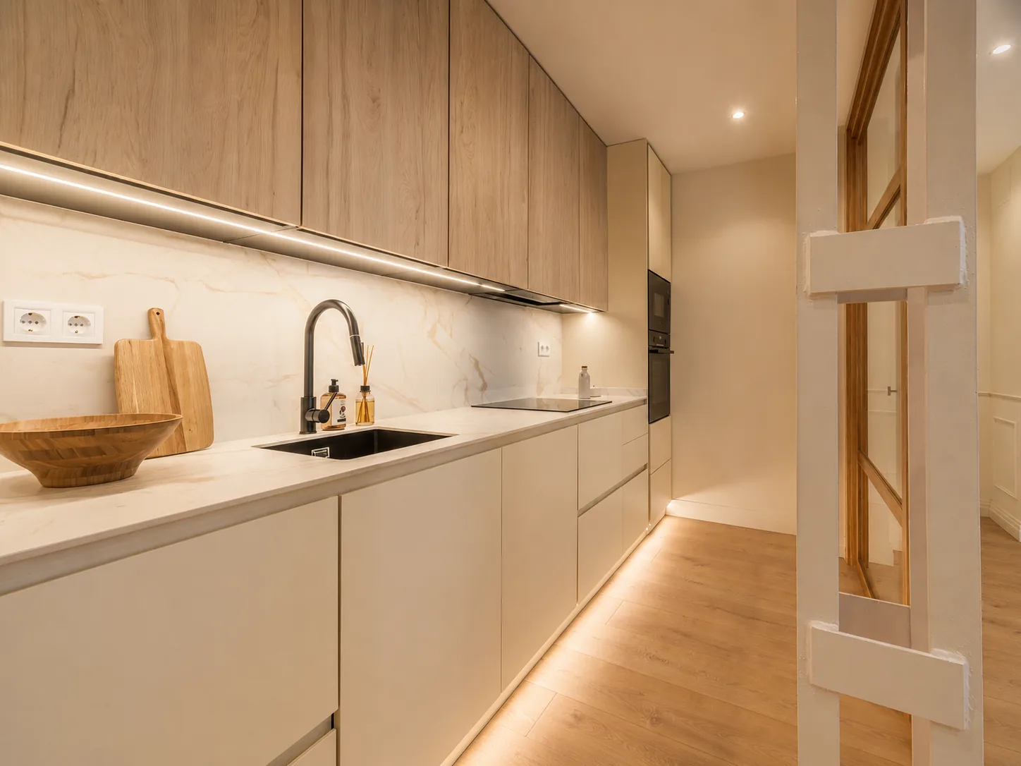 Cocina integrada en el pasillo con acabados en madera clara y crema